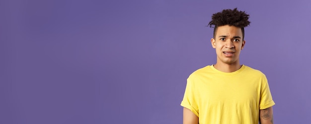 Waistup portrait of young concerned hispanic man with worried gaze looking at camera frowning being