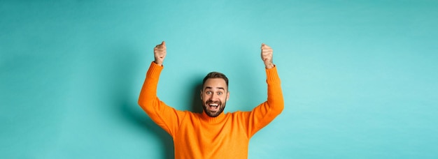 Free photo waistup shot of happy man raising hands as if holding a sign showing logo or promo banner smiling ex