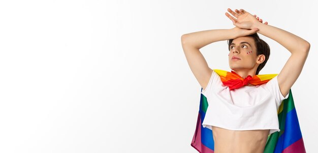 Waistup shot of sensual androgynous man wearing crop top and rainbow pride flag looking at upper lef