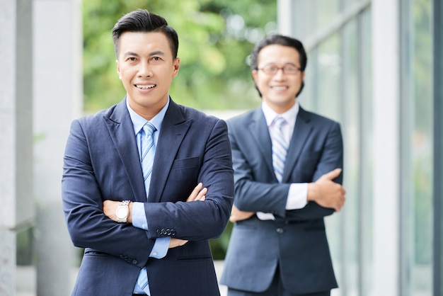 Waistup shot of two Asian businessmen standing with arms folded outdoors