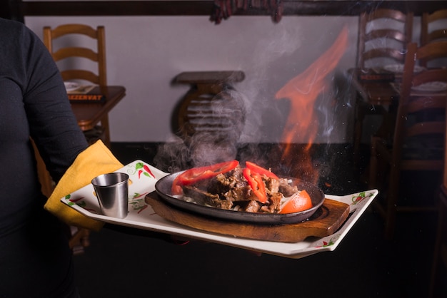 Free photo waiter carrying tray with meat on fire