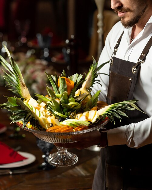 Waiter holding a platter of fruit mix with original serving