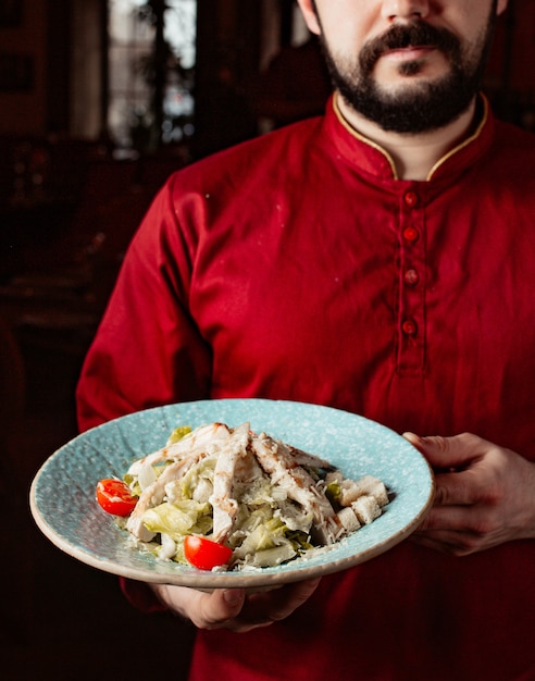 Waiter holds caesar salad with chicken lettuce cherry tomato parmesan and bread stuffing