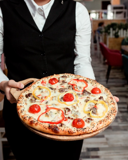 Free photo waiter holds meat pizza with yellow red bell peppers tomato and cheese