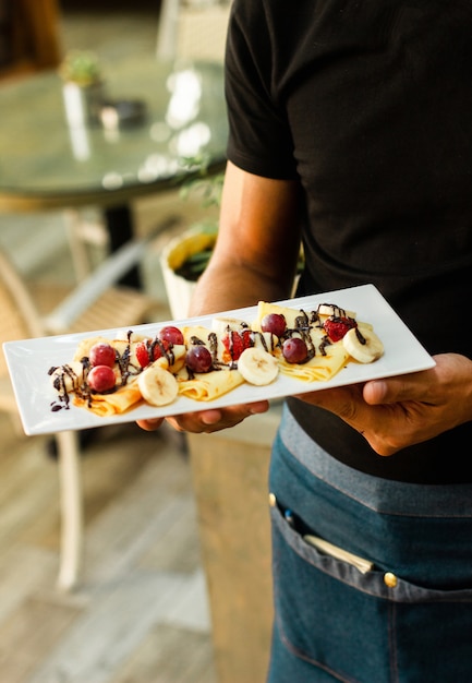 Free Photo waiter holds a serving of crepe with fruits and chocolate sauce