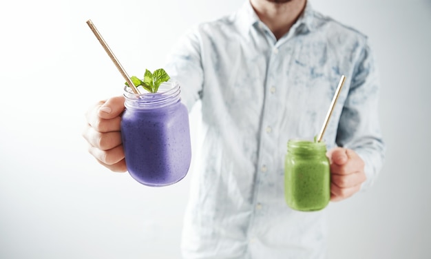 Free photo waiter offers two tasty cold smoothies from blueberry and kiwi in rustic jars with drinking straw inside