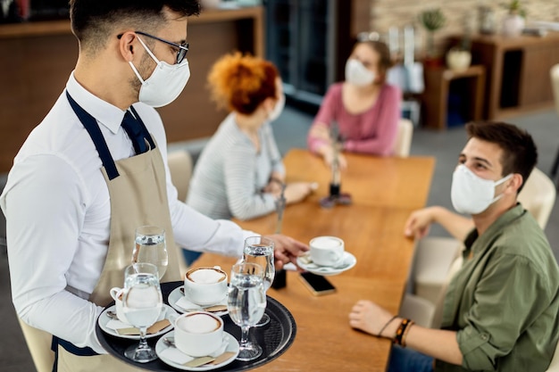 Free photo waiter serving coffee to customers while wearing a face mask due to covid19 epidemic