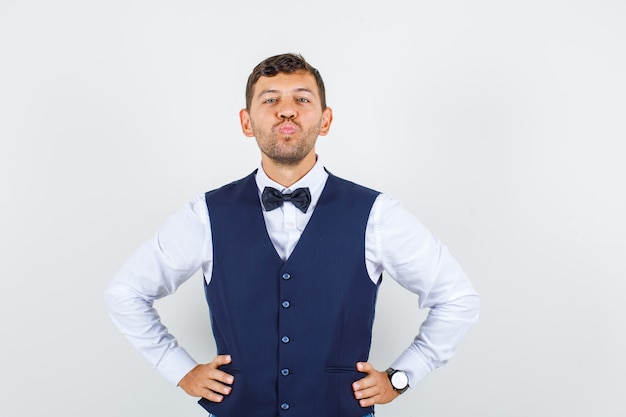 Free photo waiter in shirt, vest holding hands on waist with folded lips , front view.