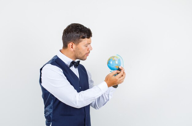 Waiter in shirt, vest holding and looking at world globe , front view.