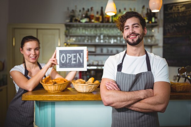 Waiter standing with arms crossed at counter in cafÃ©