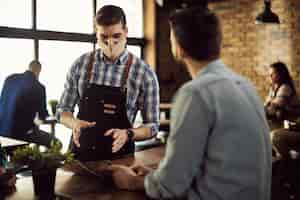 Free photo waiter wearing face mask while talking to customer in a cafe