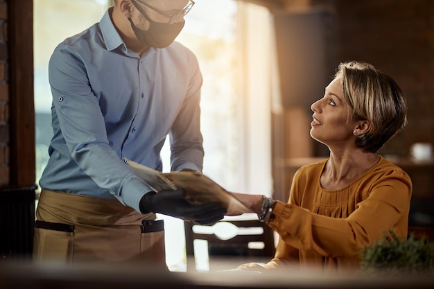 Free photo waiter wearing protective face mask and showing menu to a customer while talking to her in a cafe