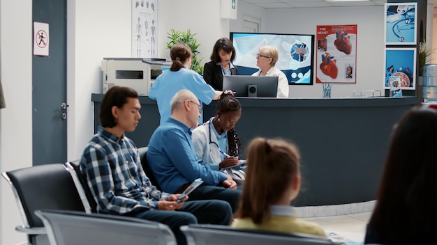 Free photo waiting room in hospital lobby with reception counter desk, diverse people waiting to attend checkup visit appointment. health care examination in emergency area at medical clinic.