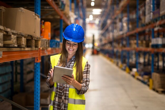 Warehouse female worker checking inventory on digital tablet in large distribution warehouse storage area