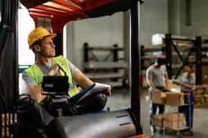 Free photo warehouse forklift driver thinking of something while going through delivery schedule in industrial building