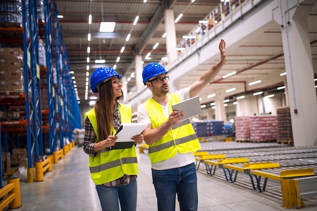 Warehouse workers consulting each other in large factory storage area