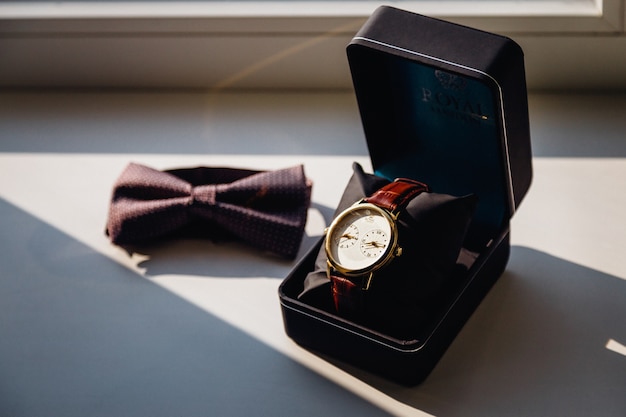 Free photo watch in black box and a bow tie lie on the white windowsill