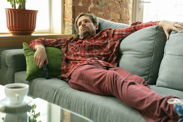 Free Photo watching tv lying on sofa. caucasian man staying at home during quarantine