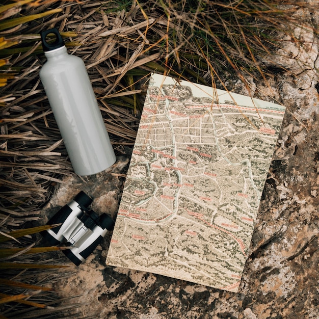 Free photo water bottle; binocular and map on rock near the grass