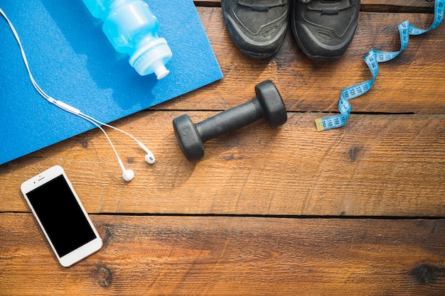 Free photo water bottle; sport shoes; earphone; cellphone; dumbbells and measuring tape on wooden background