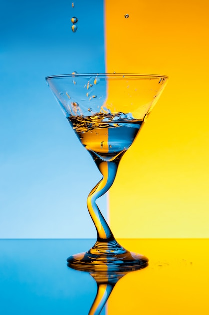 Free photo water pouring in glass over blue and yellow wall