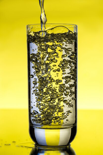 Water pouring in glass over yellow wall