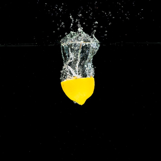 Water splash over the halved lemon over black background