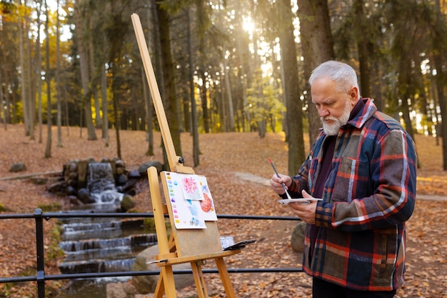 Free photo watercolor painting artist outdoors in the forest with easel and canvas