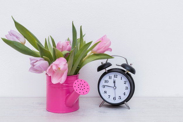 Free photo watering pot with flowers and clock