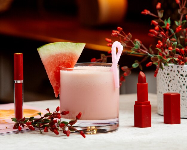 Watermelon milkshake garnished with watermelon, next to red lipstick