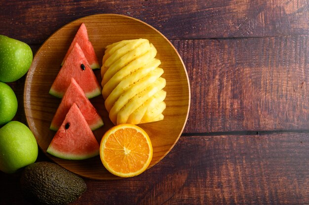 Watermelon, orange and pineapple cut into pieces on a wooden plate with apples.