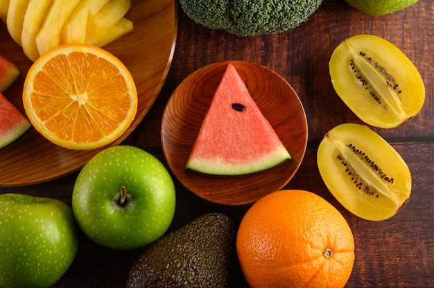 Watermelon, orange, pineapple, kiwi cut into slices with apples and broccoli on a wooden plate and wooden table.