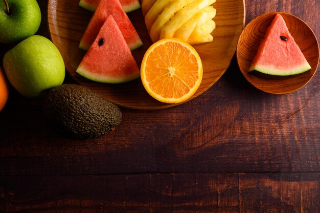 Watermelon, pineapple, oranges, cut into pieces with avocado and apples on wood table. Top view.