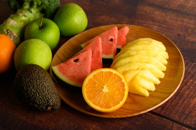 Watermelon, pineapple, oranges, cut into pieces with avocado, Broccoli and apples on wood table. Top view.