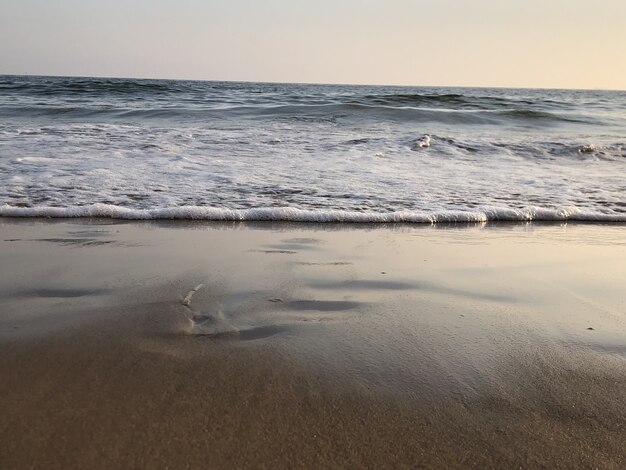 Wavy ocean hitting the sandy beach and gleaming under the colorful sky