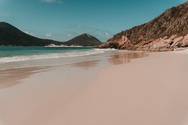 Wavy ocean hitting the sandy beach surrounded by mountains in Rio de Janeiro