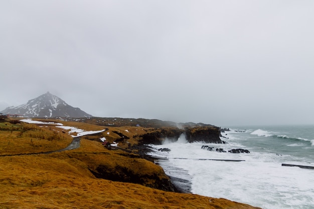 Free photo wavy sea surrounded by rocks covered in the snow and grass under a cloudy sky in iceland