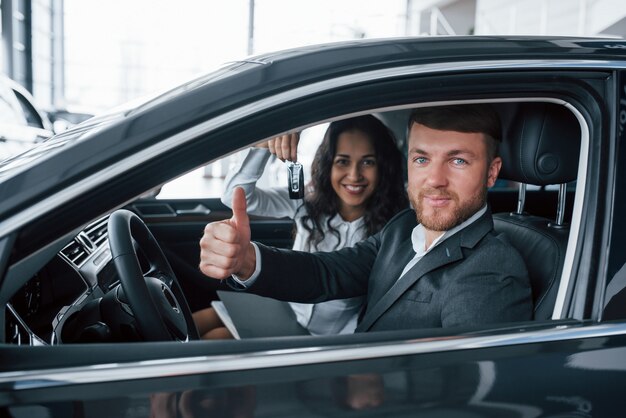 We like this. Lovely successful couple trying new car in the automobile salon