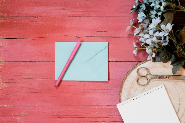 Wedding compositions with invitation envelope, flowers, a pen and scissors on a light pink wooden background