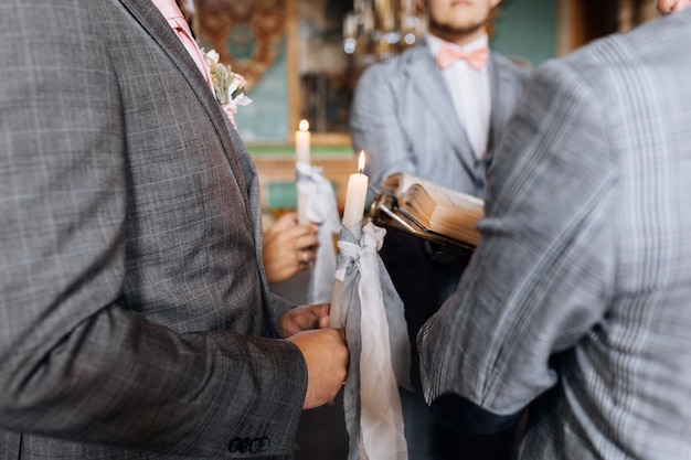 Wedding couple is holding candles with grey ribbons at the sacred wedding ceremony in the church