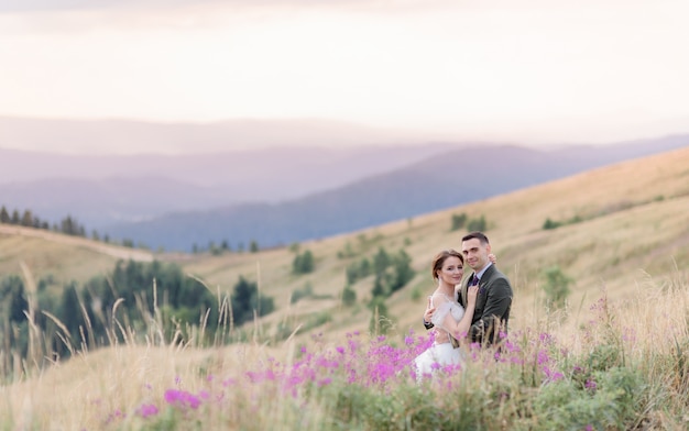 Free photo wedding couple with a picturesque mountain landscape is sitting on the meadow