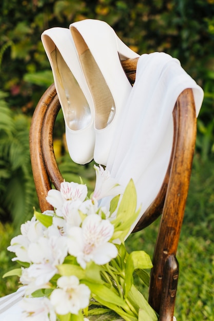 Wedding flower bouquet; high heels and scarf on wooden chair in the park