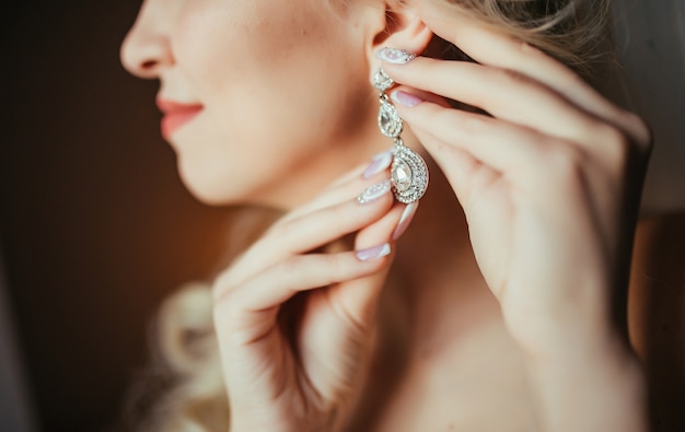 Wedding preparation. Beautiful, happy bride dresses earrings before wedding. 