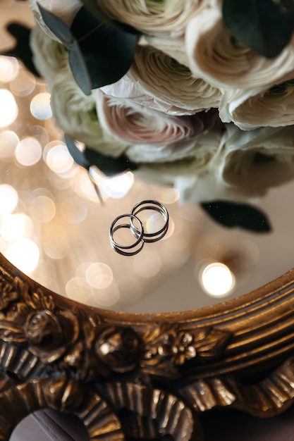 Wedding rings of the bride and groom on a mirror surface with boke near fresh flowers.