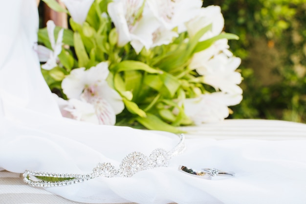 Free photo wedding rings; crown; scarf near the flower bouquet on table