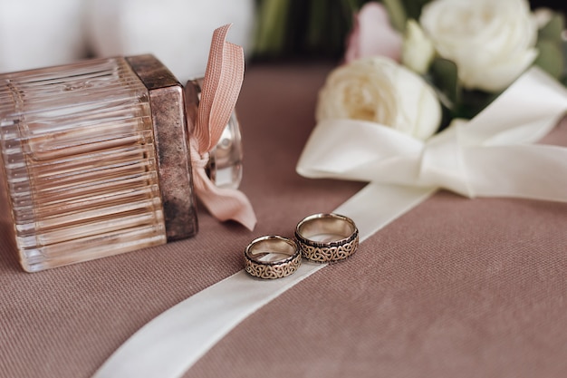 Wedding rings with engraving on the creamy ribbon, perfume and the white flowers