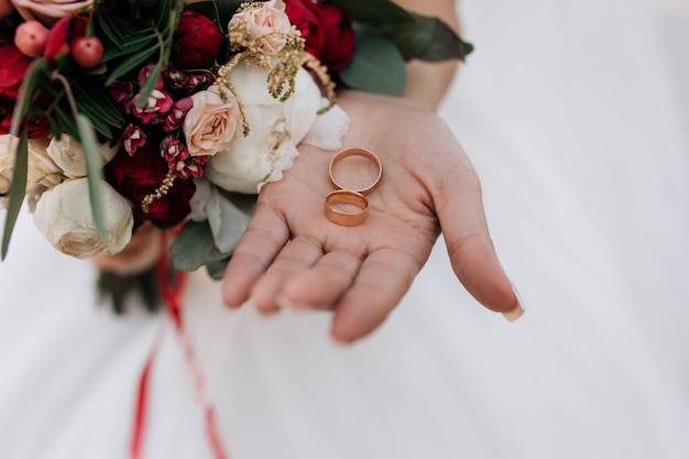 Wedding rings on the woman's hand, wedding bouquet of red and white flowers, wedding details