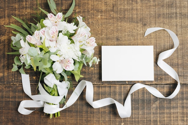 Wedding white card and peruvian lily flower bouquet tied with ribbon on wooden desk