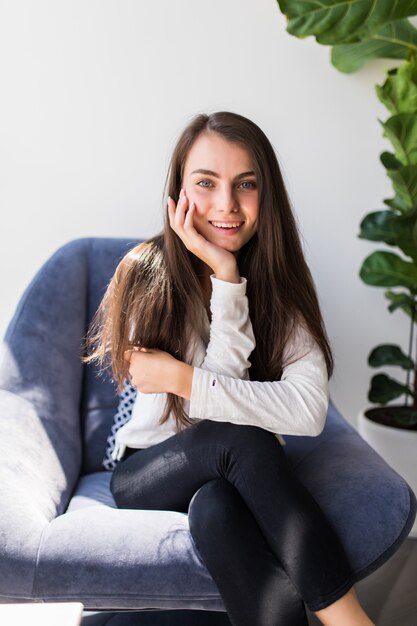 Weekends finally. Relaxed brunette girl is sitting on modern chair near the window in light cozy room at home.