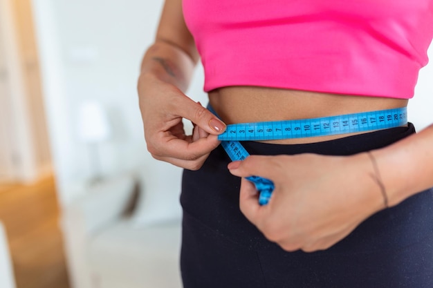 Weight Loss Concept Portrait of millennial African American lady in top bra and leggings measuring her waist using blue tape free copy space Black woman checking body parameters